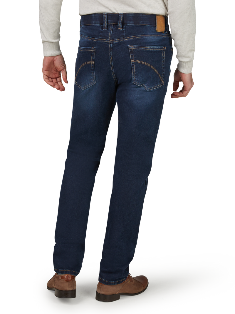 Blick auf die Rückseite einer Person, die dunkelblaue Jeans trägt. Die Jeans hat sichtbare braune Nähte, zwei Gesäßtaschen und einen braunen Lederlabel am Bund. Die Person trägt eine graue Jacke und braune Schuhe, steht auf einem hellen Boden.