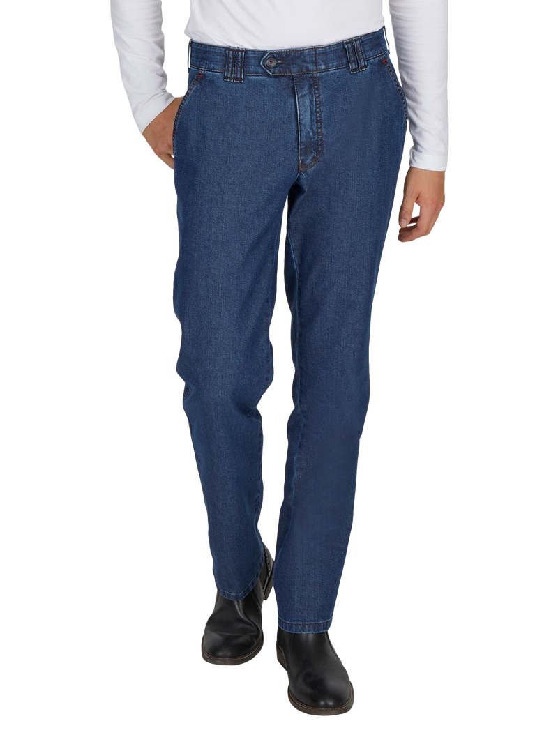 Hosenbein einer Person trägt eine dunkelblaue Jeans mit geradem Schnitt. Die Person trägt ein weißes langärmeliges Oberteil und schwarze Schuhe.