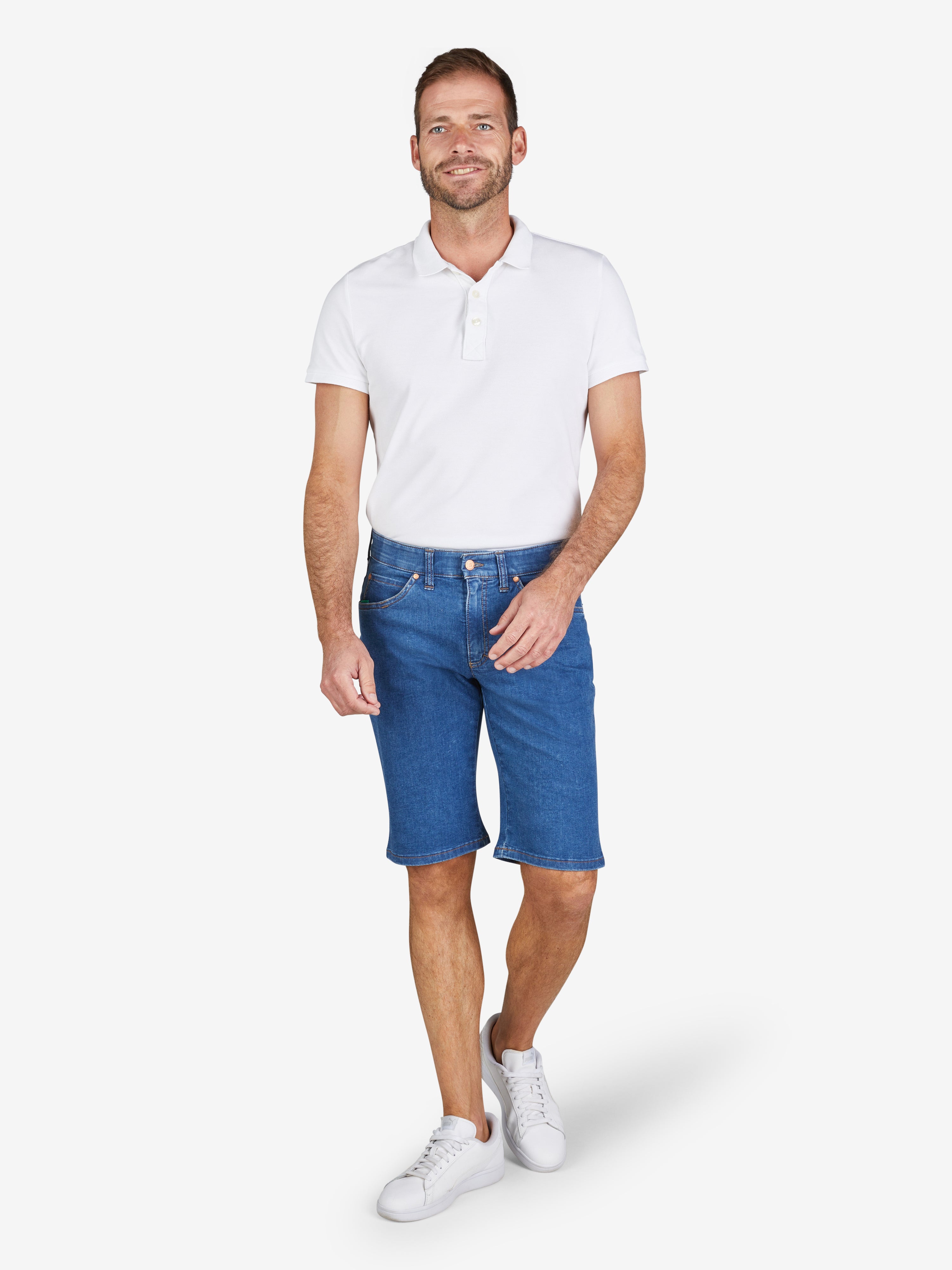 Mann trägt weiße Polo-Shirt und blaue Bermuda-Shorts aus hoch elastischem Super High Stretch-Denim mit Komfortbund, Hemdenstopper und normaler Leibhöhe. Produktbeschreibung ESPANA 6516 in jeansblau, hergestellt von Club of Comfort.