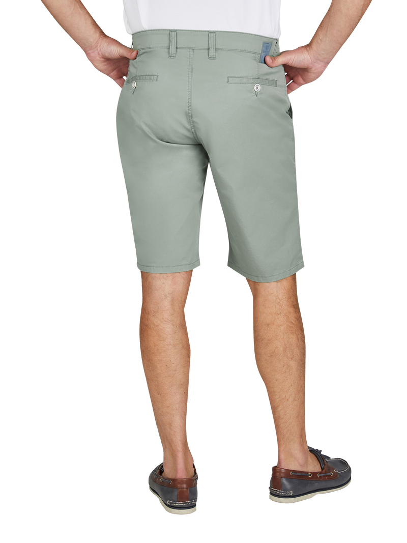 Blick auf die Rückseite eines Mannes, der eine hellgrüne kurze Hose trägt. Die Hose hat zwei Gesäßtaschen mit Knöpfen und Gürtelschlaufen. Der Mann steht mit den Händen in den Hüfttaschen, trägt braune Schuhe und ein weißes Oberteil.