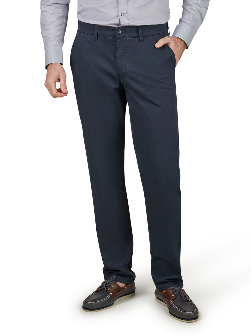 Am Bild ist die unteren Körperhalb eines Mannes zu sehen, der einen grauen Hemd und dunkle Anzughose trägt. Er hat die rechte Hand in der Hosentasche und trägt braune Halbschuhe.