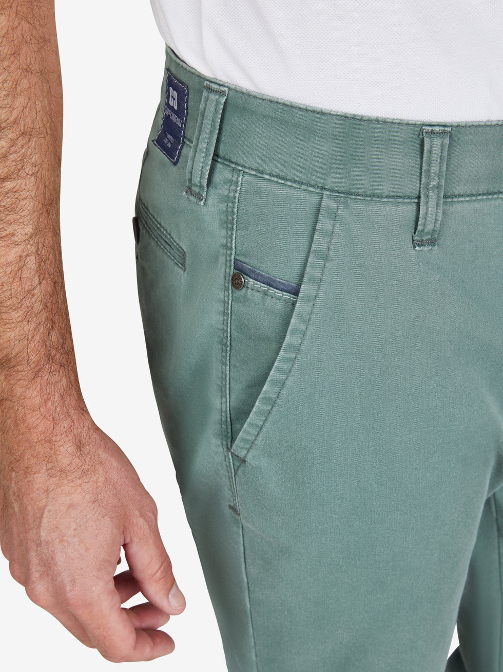 Nahaufnahme einer blaugünnen Flat Front-Hose mit elastischem Komfortbund, Hemdstopper und Münztasche rechts. Das Produkt ist leicht, aus recyceltem Baumwoll-High Stretch mit Fade Out-Färbung und Coolmax EcoMade Klimaregulierung. Marke: Club of Comfort, Modell GARVEY 7323.