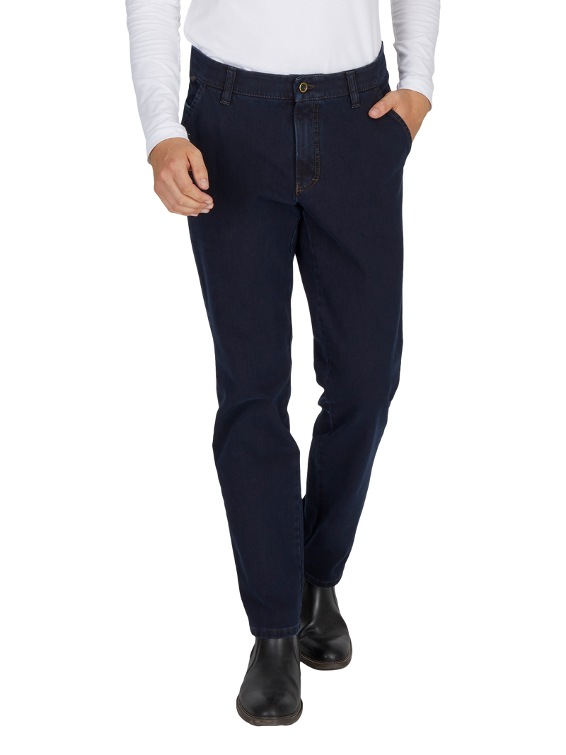 Der Bild zeigt eine Person in dunklen Jeans, die eine rechte Hand in die Hosentasche steckt und eine weiße, lange Ärmel-Hemd trägt. Die Person trägt schwarze Schuhe.