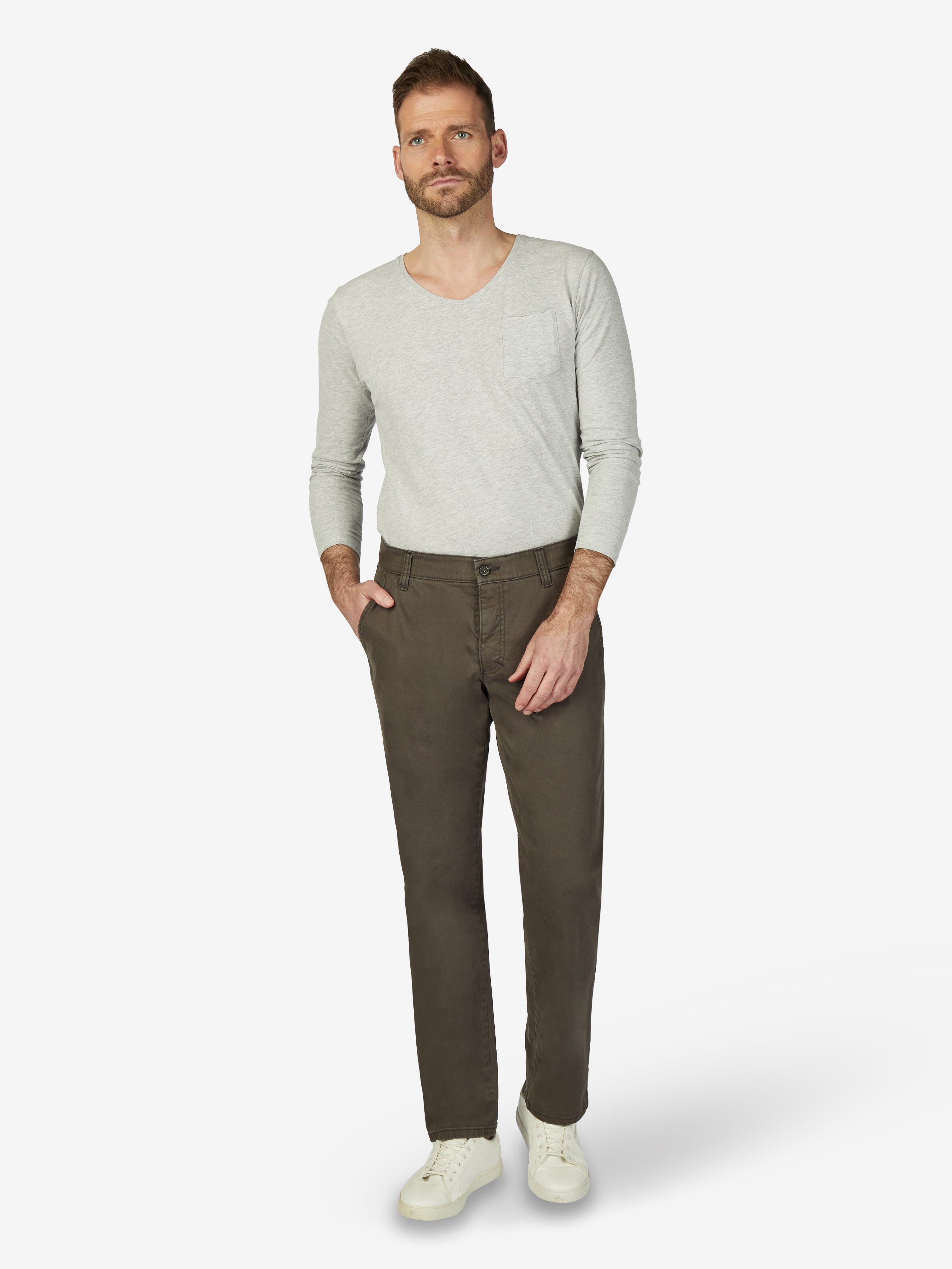 Mann trägt eine steingraue GARVEY 7612 Flat Front-Hose aus High Stretch-Baumwolle mit elastischem Komfortbund, Hemdenstopper, normaler Leibhöhe und schmaler Fußweite, kombiniert mit einem hellgrauen Pullover und weißen Sneakers, auf neutralem Hintergrund.