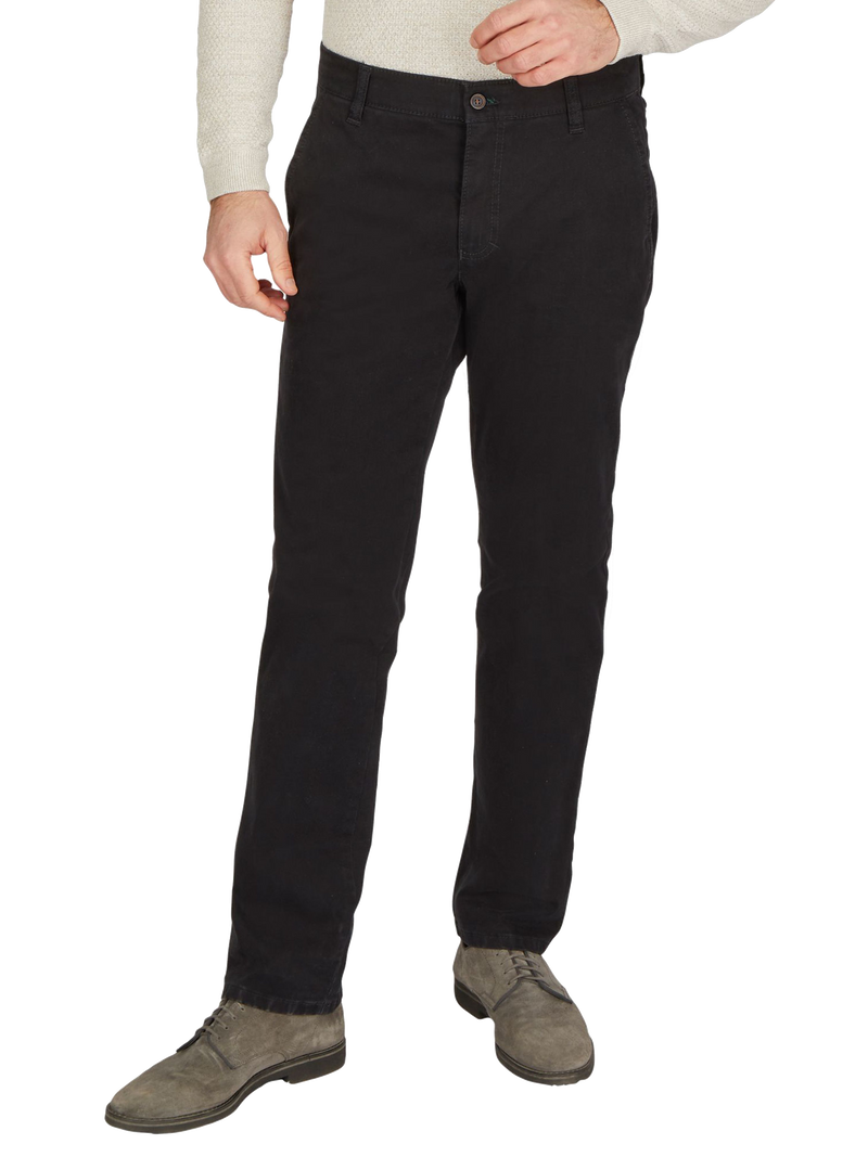 Ein Mann trägt schwarze Jeans, die leicht lockere Passform haben, mit Gürtel, auf der Hüfte sitzend, kombiniert mit einem hellen, langen Pullover und grauen Schuhe.