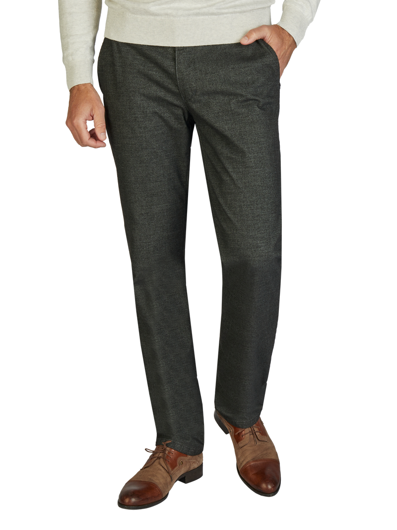 Nahaufnahme eines Mannes, der schwarze Anzughosen trägt. Er hat eine linke Hand in der Hosentasche, trägt braune Lederhalbschuhe und ein beige Mantel. Das Bild zeigt nur den unteren Bereich des Mannes.