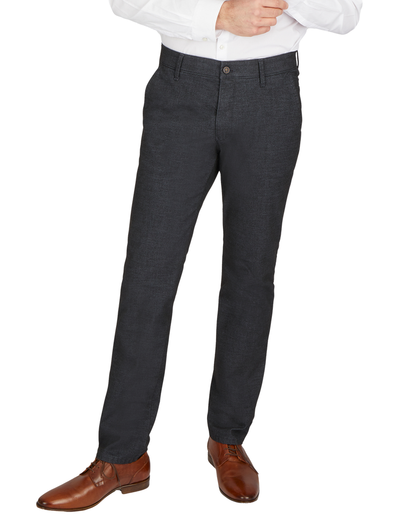 Blick auf die unteren Körperhälfte eines Mannes, der dunkle Stoffhose, braune Lederschuhe und ein weißes Hemd trägt.