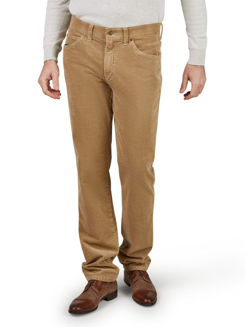 Herren trägt braune Cordhosen, die bis zu den Füßen reichen und leicht gefaltet sind. Sie trägt braune Lederschuhe und ein hellgraues Hemd.