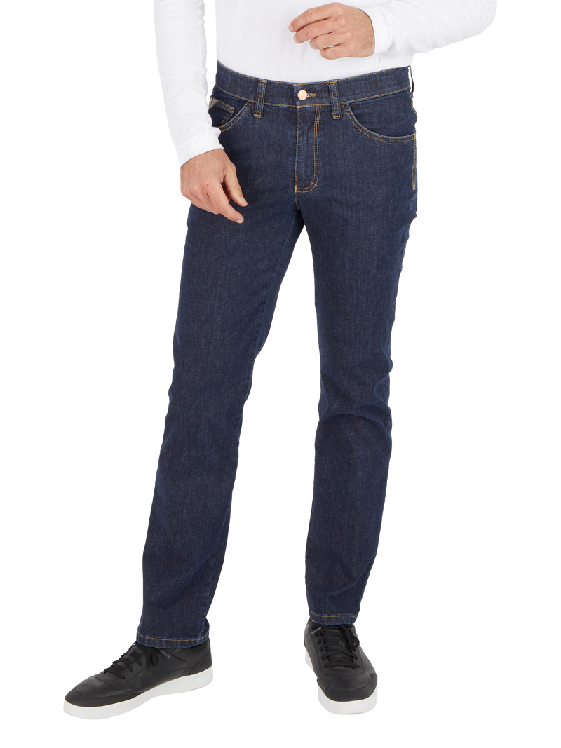 Nahaufnahme einer Person in dunklen Jeans, mit weißem Oberteil und schwarzen Sportschuhen, die locker eine Hand in die Tasche steckt.