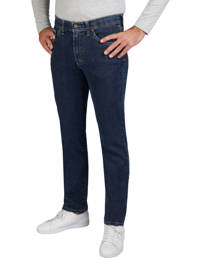 Nahaufnahme der unteren Körperhälfte einer Person, die dunkle Jeans, weiße Sneakers und ein langärmeliges hellgraues Oberteil trägt. Die Person hat die Hände in die Taschen gesteckt, die Beine leicht auseinander.