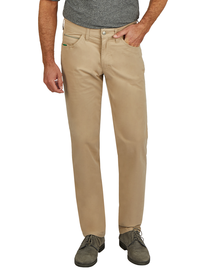 Nahaufnahme eines Mannes, der eine beige Chinohose trägt. Der Mann trägt ein graues T-Shirt und graue Schuhe. Die Hose hat Taschen an der Seite und einen Reißverschluss mit Knopf vorne. Seine rechte Hand ist in der Hosentasche, die linke hängt entspannt an der Seite.
