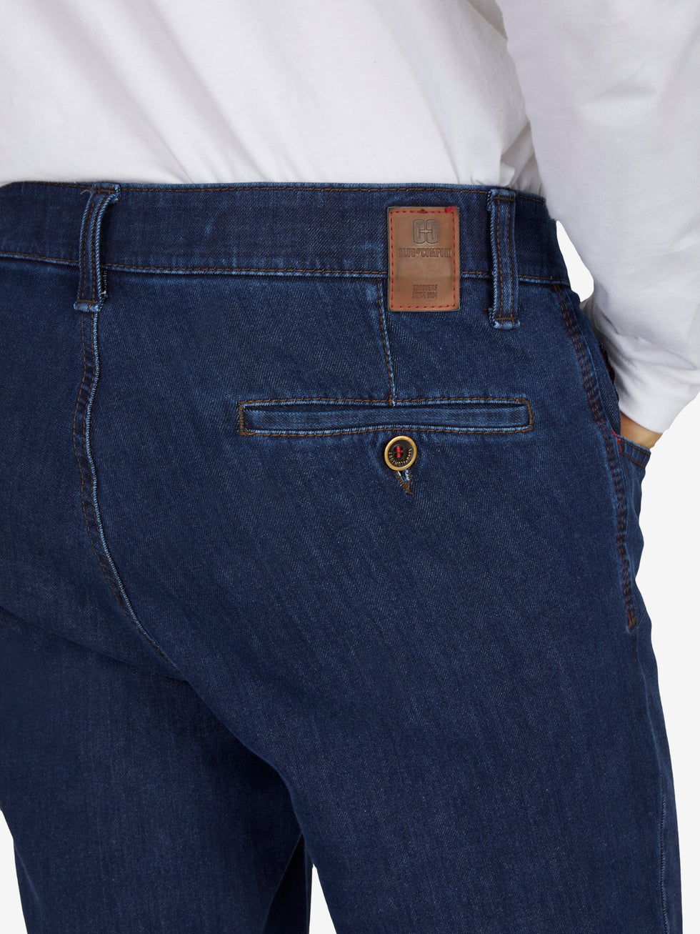 Nahaufnahme einer dunkelblauen Jeanshose "MARVIN 7054" in Jeansblau, mit elastischem Comfortbund, Hemdstopper und Swing-Pockets. Die Hose hat eine normale Leibhöhe, schlanke Beinlinie, und ist aus hochelastischem Bi-Stretch-Denim gefertigt. Markenlabel von "Club of Comfort" sichtbar.