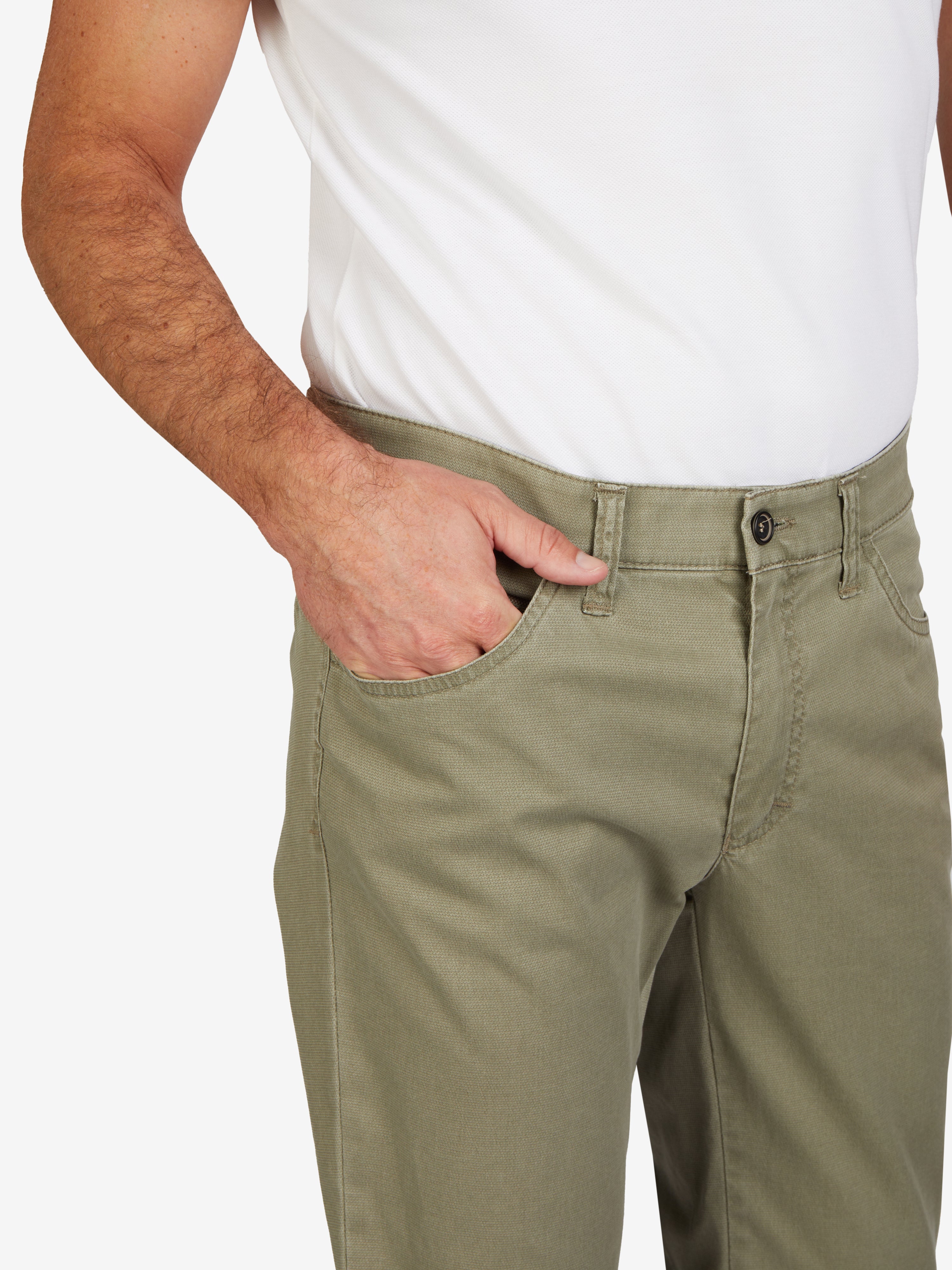 Nahaufnahme einer grünen, modifizierten 5-Pocket-Hose namens MARVIN 7907 in Khaki. Die Hose hat einen elastischen Comfortbund, Hemdstopper, eine Münztasche mit Kontrast, normaler Leibhöhe, schmales Bein, zeigt eine seitliche Tasche mit Hand darin, hergestellt aus hochelastischer High Stretch-Baumwolle. Produkt von Club of Comfort, für Frühjahr/Sommer, waschbar, nachhaltig und made in Green by Oeko-Tex.