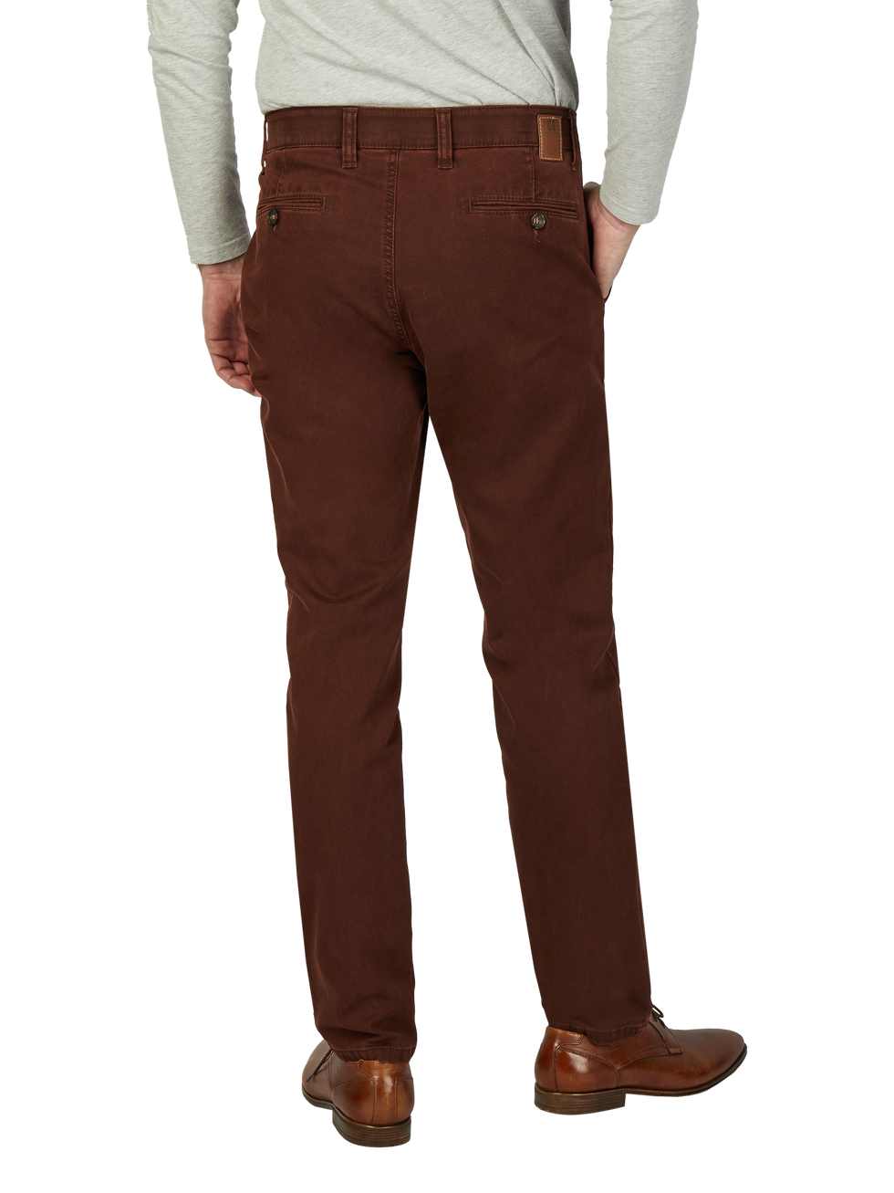 Blick auf die Rückseite eines Mannes, der braune Chino-Hosen trägt, die am Bund Gürtelschlaufen haben. Er trägt eine helle, langärmelige Shirt, die bis über den Hosenbund reicht, und braune Lederschuhe.