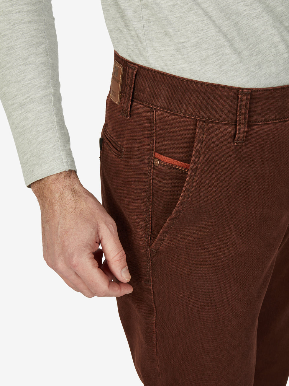 Nahaufnahme einer ziegelroten Garvey 7218 Flat Front-Hose aus Baumwolle mit elastischem Komfortbund, Hemdenstopper und stilvoller Münztasche. Hose mit schmalem Beinform, hoher Stretch-Qualität, Made in Green by Oeko-Tex, für Herbst/Winter.