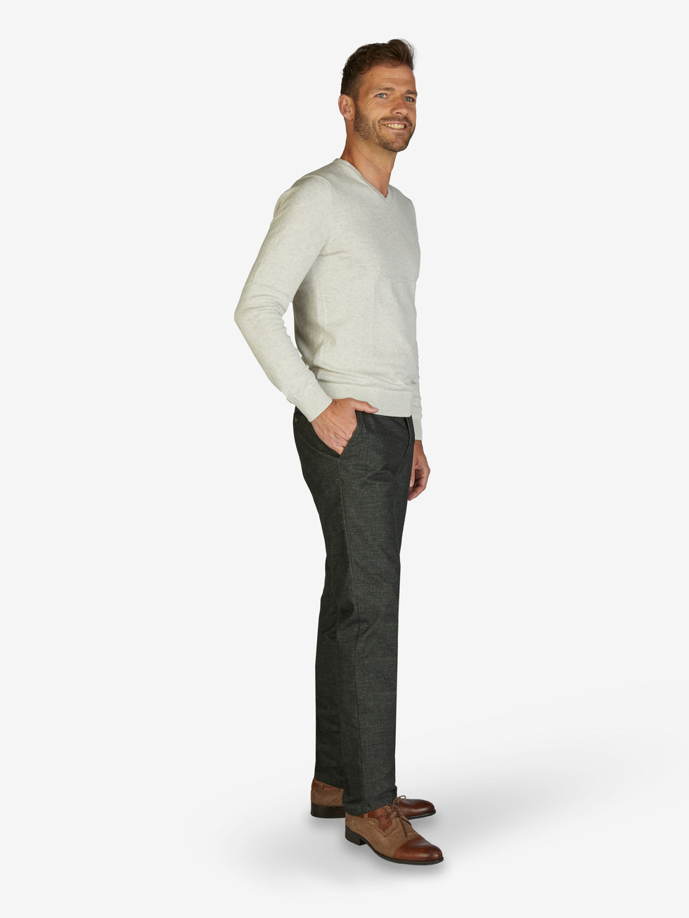Mann trägt eine dunkelgraue, melierte Flat Front-Hose mit elastischem Komfortbund, Hemdstopper und schmaler Fußweite, kombiniert mit einem hellgrauen Pullover, auf weißem Hintergrund.