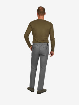 Ein Mann steht mit Rückenansicht, trägt eine grau-graue Flat Front-Hose mit elastischem Komfortbund und Hemdenstopper, kombiniert mit einem grünen Longsleeve. Die Hose ist aus leichtem Baumwoll-High-Stretch gefertigt, mit schmaler Fußweite, normaler Leibhöhe und clearem Look.