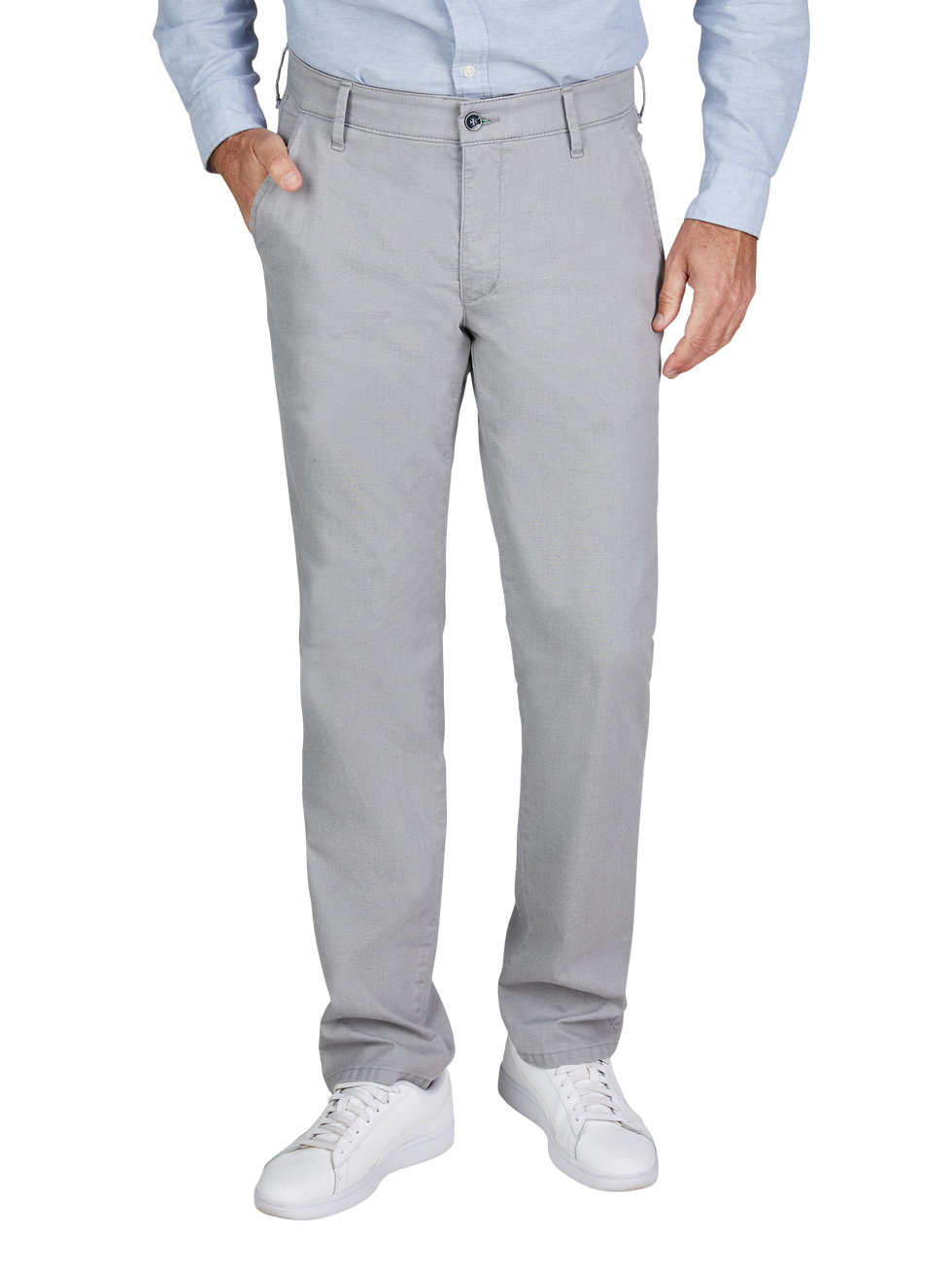 Mann trägt helle graue Hosen, eine hellblaue Hemd und weiße Sneakers. Der Mann hat eine Hand in der Hosentasche.