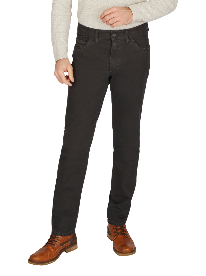 Nahaufnahme eines Mannes, der schwarze Jeans trägt, die bequem sitzen und detailliert den Bund, die Taschen und die Passform zeigen. Er trägt braune Lederschuhe und ein helles, langärmeliges Oberteil.