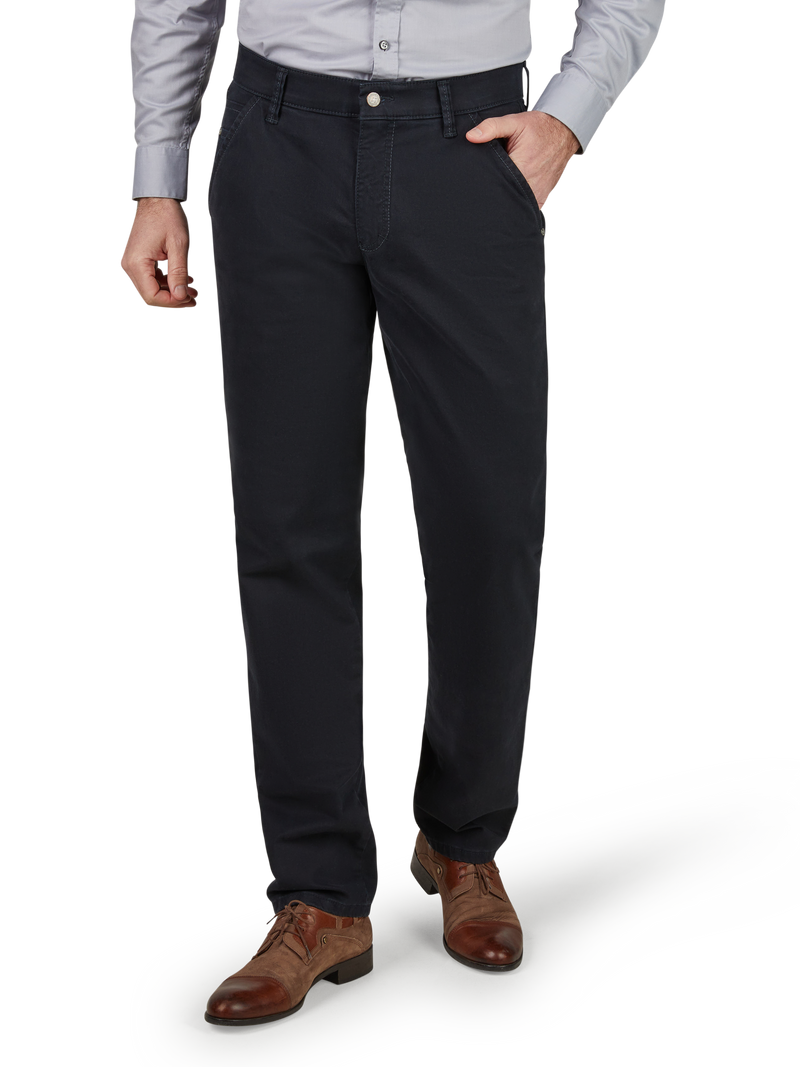 Nahaufnahme eines Mannes, der schwarze Stoffhose und braune Lederschuhe trägt. Er steht mit einer Hand in der Hosentasche, ein Hemd ist teilweise sichtbar. Das Bild fokussiert auf den unteren Brust- und Beinbereich, vor neutralem Hintergrund.