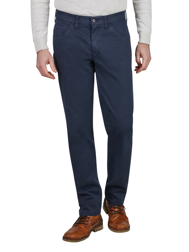 Blick auf die unteren Körperhälfte eines Mannes, der eine graue Strickjacke, dunkle Jeans, braune Lederstiefel trägt. Die Jeans sind gerade geschnitten, mit klassischen Taschen und Gürtelschlaufen.